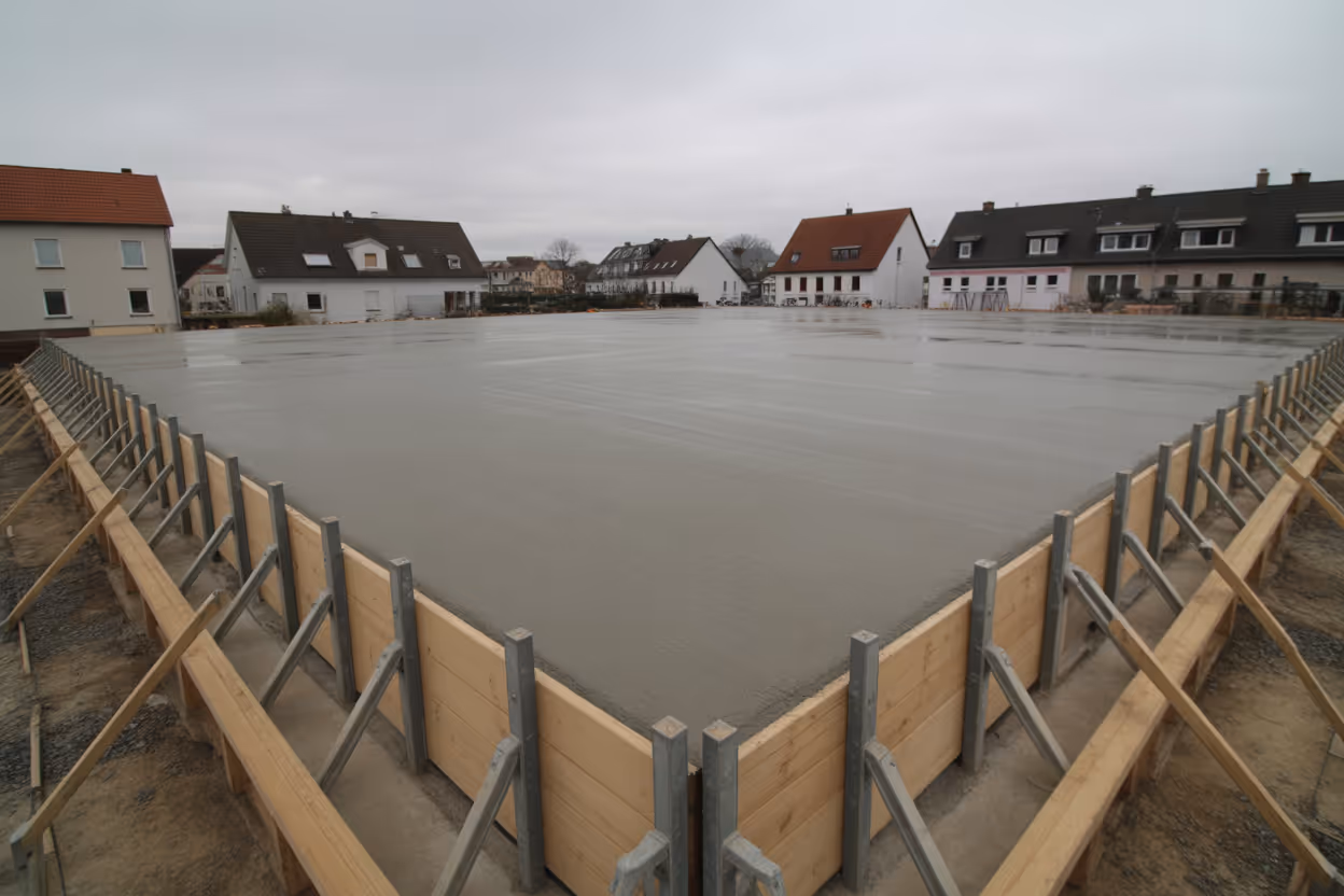 Frisch betoniertes Fundament auf einer Neubau-Baustelle in Hamburg mit Wohnhäusern im Hintergrund